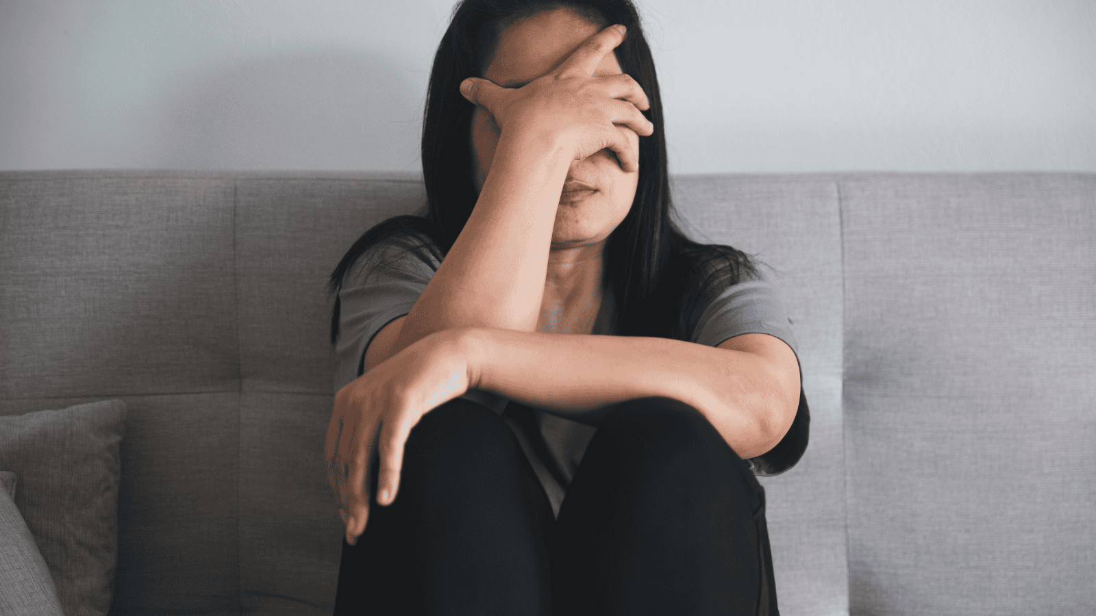 A depressed woman is sitting on the floor and hiding her face