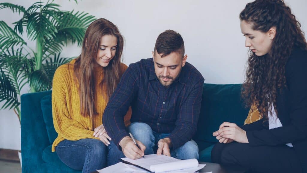 A couple reviews and signs paperwork with an advisor on a sofa