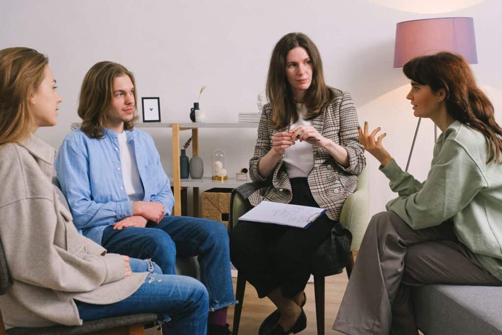 A therapist leads a small group session on sofas in a warm room.
